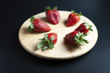 Ahşap döner tepside taze çilek ve siyah arka plan.