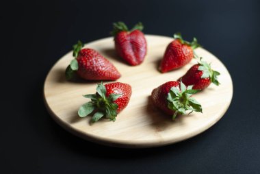 Ahşap döner tepside taze çilek ve siyah arka plan.