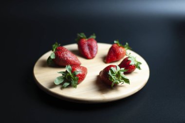 Ahşap döner tepside taze çilek ve siyah arka plan.