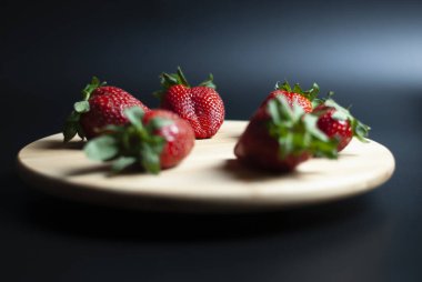 Ahşap döner tepside taze çilek ve siyah arka plan.