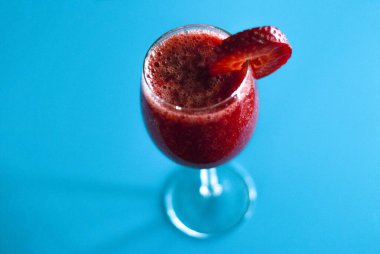 Bir fincan doğal kırmızı ve taze çilek suyu sıkılmış el ve açık mavi arka planda bir dilim.