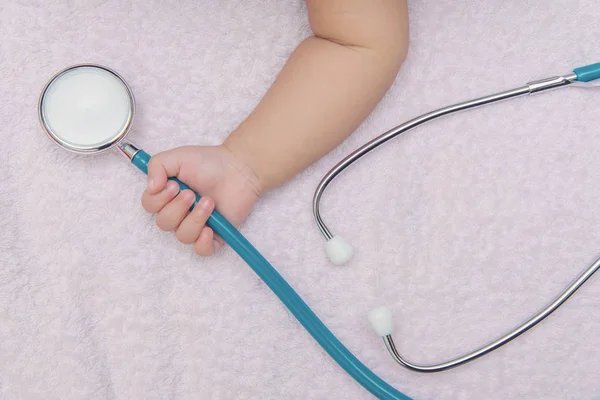 Instrumentos médicos estetoscopio en la mano de la niña recién nacida —  Fotos de Stock