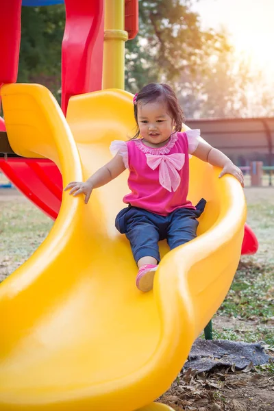 Niña jugando en un tobogán en el parque infantil —  Fotos de Stock