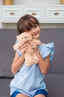 Oyuncak ayı ile evde oturma odasında oynayan kız çocuk