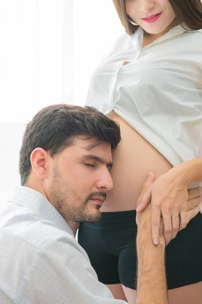 Pregnant woman and her handsome husband is listening to baby in — Stock Photo, Image