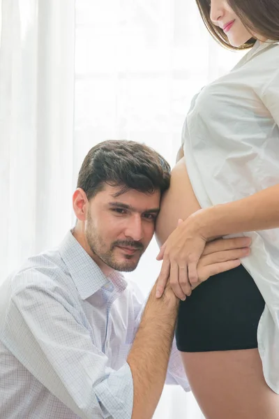 Pregnant woman and her handsome husband is listening to baby in — Stock Photo, Image
