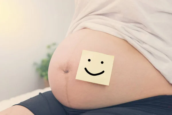 Беременная женщина с бумагой улыбки на животе — стоковое фото