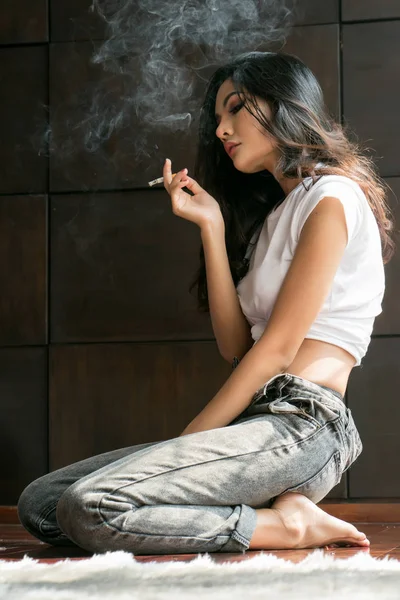 Retrato de una joven atractiva fumando un cigarrillo en la habitación . — Foto de Stock