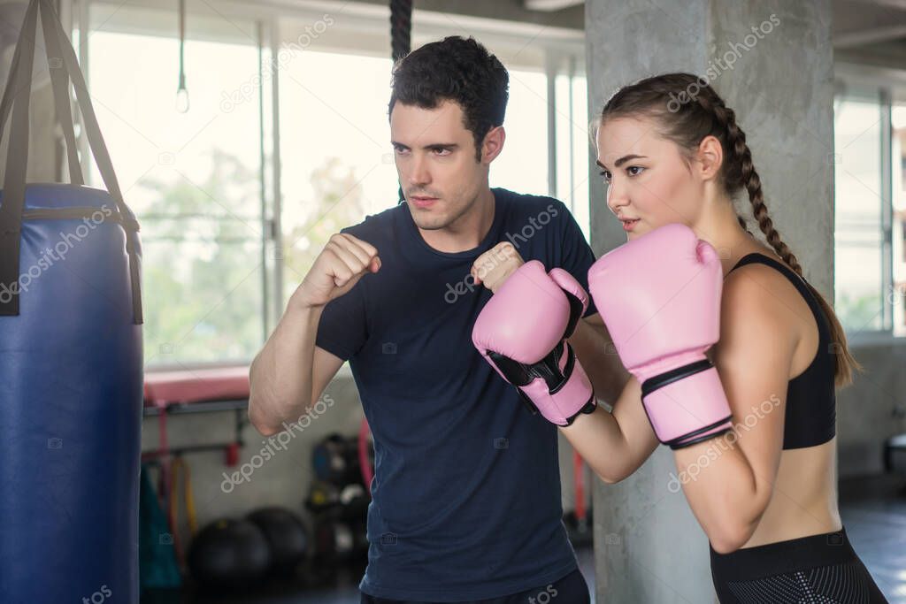 Handsome man beautiful sports woman in boxing gloves punching bags exercise in fitness gym.