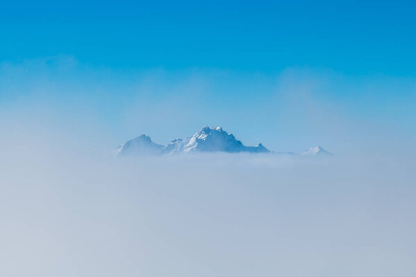 summit of Pilatus mountain sticking out of sea of fog with blue 