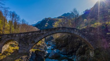 İsviçre 'deki Maggia Vadisi' nde sabah ışığında nehir ve mavi gökyüzü olan antik taş köprü.