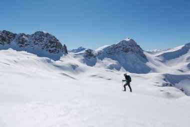 Kar ayakkabılı kadınlar, Arosa yakınlarındaki Schanfigg 'de mavi gökyüzü ile karlı kış manzarasında yürüyorlar.