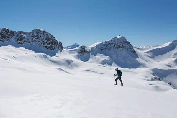 Kar ayakkabılı kadınlar, Arosa yakınlarındaki Schanfigg 'de mavi gökyüzü ile karlı kış manzarasında yürüyorlar.