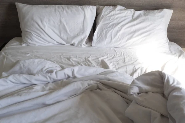 Yatakta yapılmamış beyaz yastık ve battaniye. Kullanıldıktan sonra dağınık yatak. Kırışık beyaz yatak, yastık ve çarşaflar.