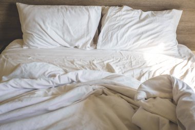 Tatilde dağınık, rahat beyaz yatak çarşafları ve yastık hayatı. Beyaz buruşuk çarşaflı dağınık bir yatak ve otel odasında iki dağınık yastık. Gevşemek için hafta sonu tatili pazar arkaplanı
