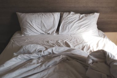 Tatilde dağınık, rahat beyaz yatak çarşafları ve yastık hayatı. Beyaz buruşuk çarşaflı dağınık bir yatak ve otel odasında iki dağınık yastık. Gevşemek için hafta sonu tatili pazar arkaplanı