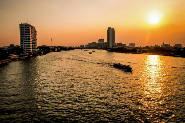 Scene of the beautiful sights seeing of Chao Phraya River with long tail boat and building around. Experience the exotic Bangkok by sunset .beautiful orange sky. Taking from Bridge cross over river