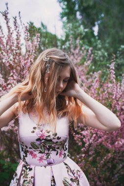 Üzerinde mehendi olan narin elbiseli bir kız, çiçek açmış bademler içinde.