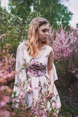 Üzerinde mehendi olan narin elbiseli bir kız, çiçek açmış bademler içinde.