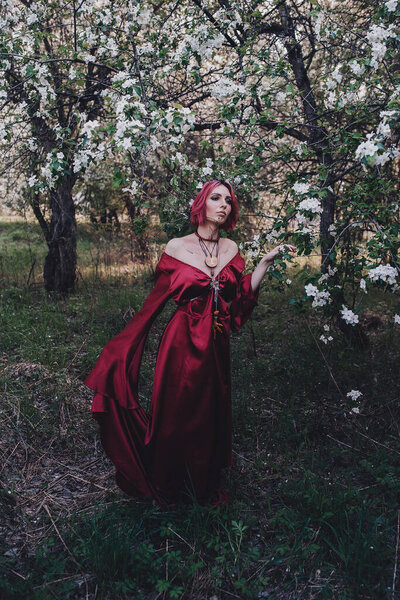 Girl in red and red hair in the form of a druid in apple trees