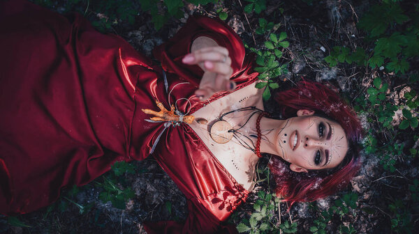 Girl in red and red hair in the form of a druid in apple trees
