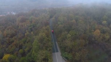 Ormanda sisli yolda ilerleyen kırmızı otobüs. Drone, Forest Road 'daki kamyonu takip ediyor.