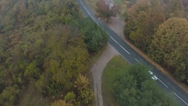 Drone goni biały samochód jadąc po mglistej asfaltowej drodze w górach — Wideo stockowe