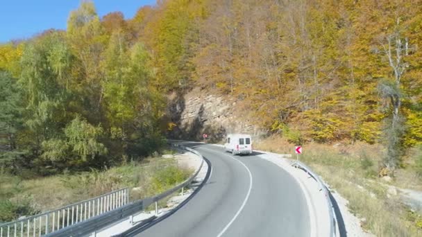 Van branca, caminhão de transporte dirigindo na estrada da montanha sinuosa em dia ensolarado. Floresta dourada do lado da estrada — Vídeo de Stock