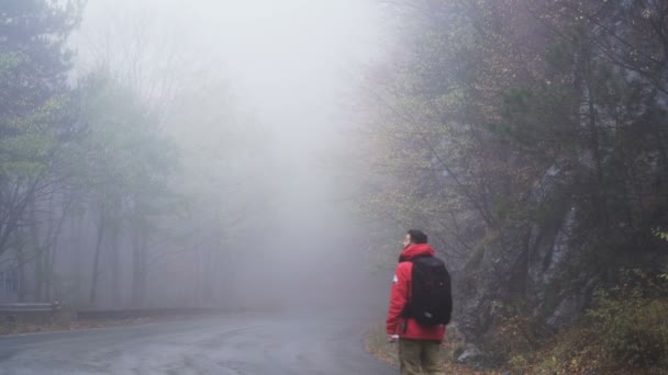 Homem caminhando em uma estrada de montanha com um monte de nevoeiro em dia chuvoso. Perdido, conceito errante — Vídeo de Stock