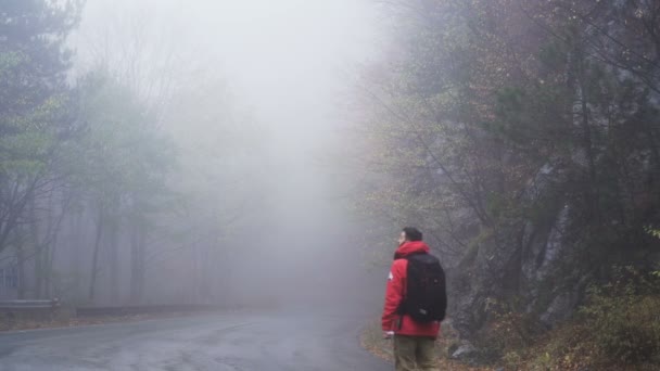 Un hombre caminando por un camino de montaña con mucha niebla en un día lluvioso. Concepto perdido y errante — Vídeos de Stock