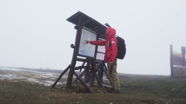 Seitenansicht eines männlichen Touristen, der oben auf dem Berg steht und den Weg sucht. Mann deckt sich vor dem Regen — Stockvideo