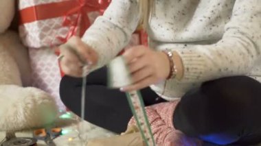 Noel süveteri giymiş hamile bir kadın, Noel hediyelerine yeşil fiyonk bağlıyor.