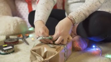 Hamile bir kadın Noel hediyelerini paketleyip bağlıyor ve yerde oturuyor.