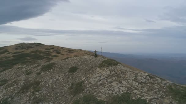 Erkek turist, dağın tepesinde, panoramik manzarayı izlerken, tasasız bir şekilde kollarını kaldırıyor. — Stok video