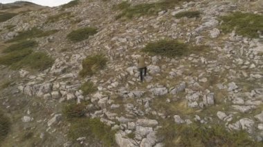 Erkek turist keskin kaya zirvesinde yürür. Yeşil ceketli yalnız yürüyüşçü manzaranın tadını çıkar..