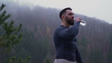 Kaslı göğsü olan genç sakallı adam eğitimden sonra şişeden su içiyor.