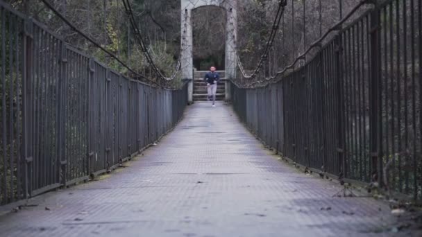 Corredor masculino con auriculares rojos corriendo en puente colgante de metal — Vídeo de stock