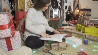 Hamile bir kadının etrafında Noel ışıkları parlıyor. Kitap okuyan genç bir kadın kalın bir kazak giyiyor.