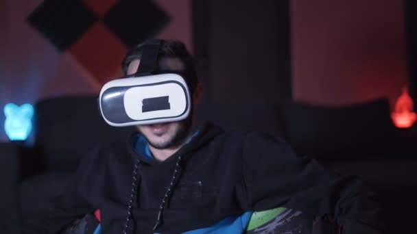 Hombre sentado en el sofá en casa jugando juegos y viendo películas con gafas VR — Vídeos de Stock