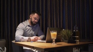 Büyük saatli sakallı işadamı gece geç saatlerde kafede çalışırken not alıyor.