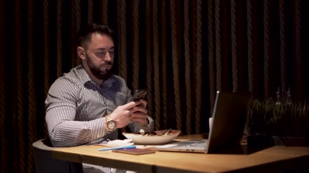 家でテーブルの上に座っている間、彼の電話で働いている黒いひげを持つ男性ビジネスマン — ストック動画