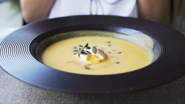 Frau in weißem Kleid sitzt auf Stuhl und wartet darauf, dass ihre Kürbiscremesuppe kälter wird — Stockvideo