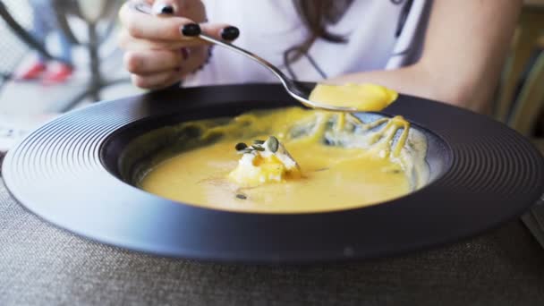 Siyah tırnaklı bir kadın restoranda siyah kâse ya da tabaktan balkabağı kremalı çorba yiyor. — Stok video