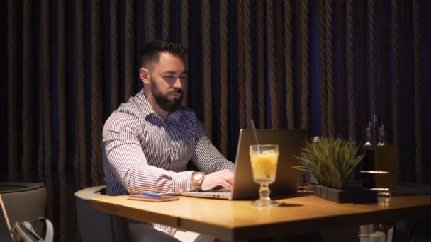 Joven hombre de negocios barbudo serio que trabaja en el proyecto con el ordenador portátil en la oficina loft por la noche . — Vídeo de stock