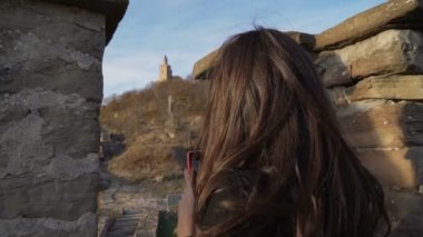 Güzel kahverengi saçlı genç bir kadın tatildeyken cep telefonuyla fotoğraf çekiyor.