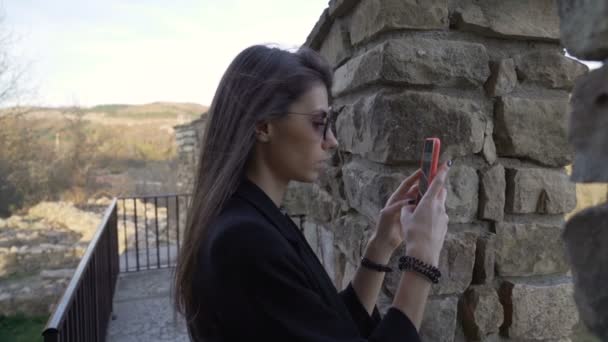 Вид сбоку молодой красивой брюнетки в солнцезащитных очках, фотографирующей и снимающей видео со смартфона — стоковое видео