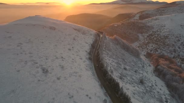 Drohne folgt Auto durch verschneite Bergstraße bei Sonnenuntergang — Stockvideo