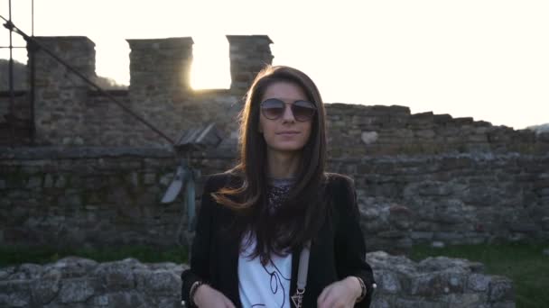 Underbar brunett med solglasögon leende och poserar mot medeltida fäste i bakgrunden — Stockvideo
