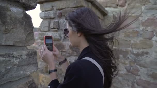 Toeristisch meisje kijkt door middeleeuwse vestingmuur en maakt foto 's van het panoramische uitzicht — Stockvideo