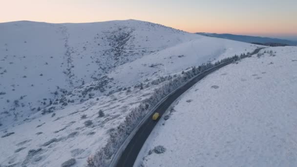 Drone sarı minibüsü gün batımında gökyüzü olan güzel karlı dağ yolunda takip ediyor. — Stok video